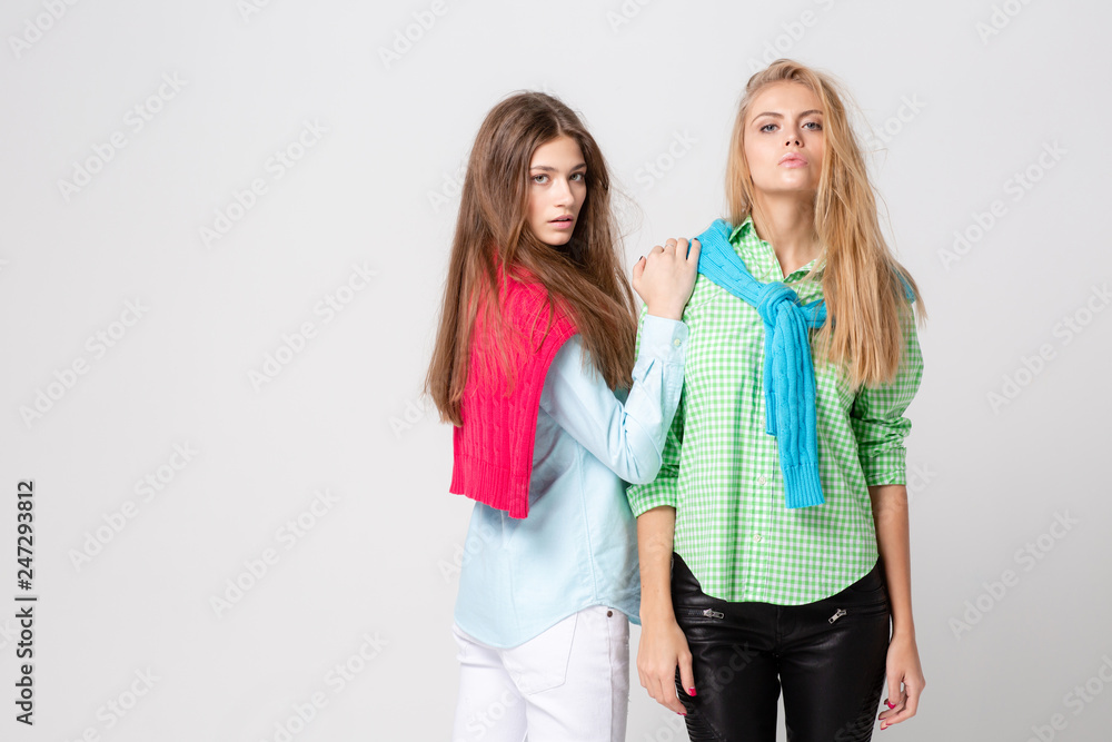 happy girlfriends women in shirts and a sweater on his shoulders. Fashion spring image of two sisters. Colorful colors clothes. Models with Blonde and light brown hair. Looking at camera . happy girlfriends women in shirts and a sweater on his shoulders. Fashion spring image of two sisters. Colorful colors clothes. Models with Blonde and light brown hair. Looking at camera .