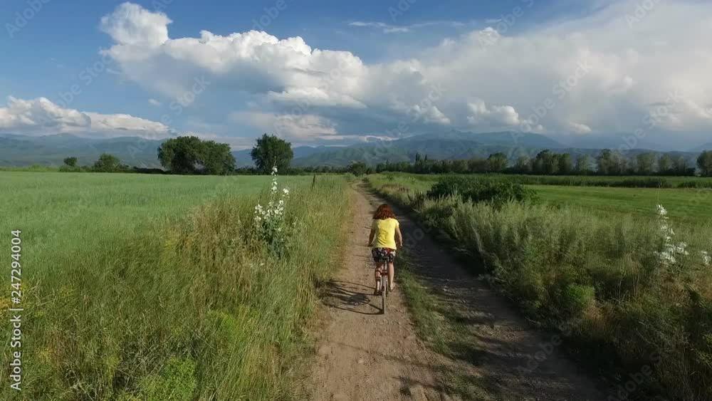 A woman riding a bike on rural road. Video from the air. Beautiful scenery of the mountains and fields. Kazakhstan, Almaty. In summer. A woman riding a bike on rural road. Video from the air. Beautiful scenery of the mountains and fields. Kazakhstan, Almaty. In summer.