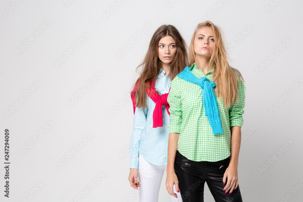 happy girlfriends women in shirts and a sweater on his shoulders. Fashion spring image of two sisters. Colorful colors clothes. Models with Blonde and light brown hair. happy girlfriends women in shirts and a sweater on his shoulders. Fashion spring image of two sisters. Colorful colors clothes. Models with Blonde and light brown hair.