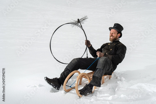 Symbolbild für guten Rutsch ins neue Jahr, Schornsteinfeger auf Holzschlitten im Schnee