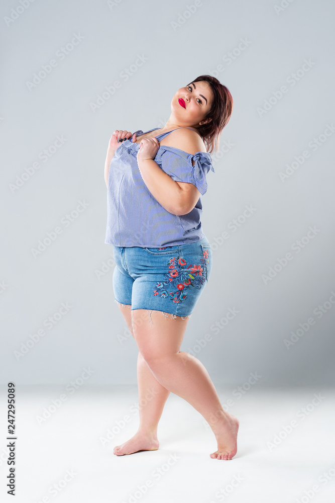 Plus size fashion model in jean shorts fat woman on gray