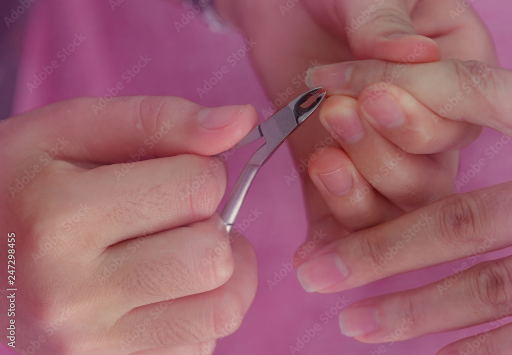 Woman receiving fingernail manicure service by professional  manicurist at nail salon. Beautician use clipper cleaning and cutting cuticle at nail and spa salon. Hand and nail therapy by therapist.