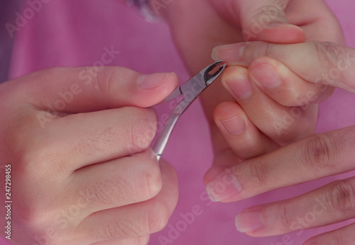 Woman receiving fingernail manicure service by professional  manicurist at nail salon. Beautician use clipper cleaning and cutting cuticle at nail and spa salon. Hand and nail therapy by therapist.