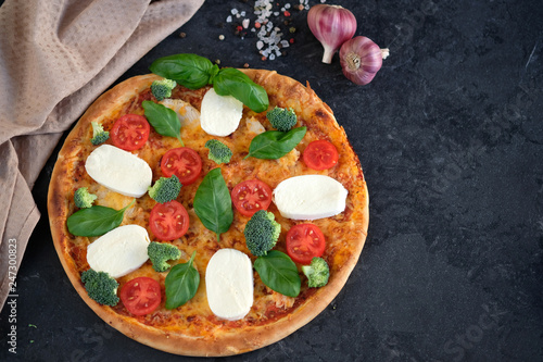 Italian pizza with Mozzarella cheese, tomatoes, broccoli, Spices and fresh basil. Pizza and kitchen napkin near, on black stone background