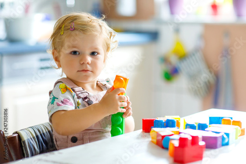 Adorable toddler girl playing with educational toys in nursery. Happy healthy child having fun with colorful different plastic blocks at home. Cute baby learning creating and building.