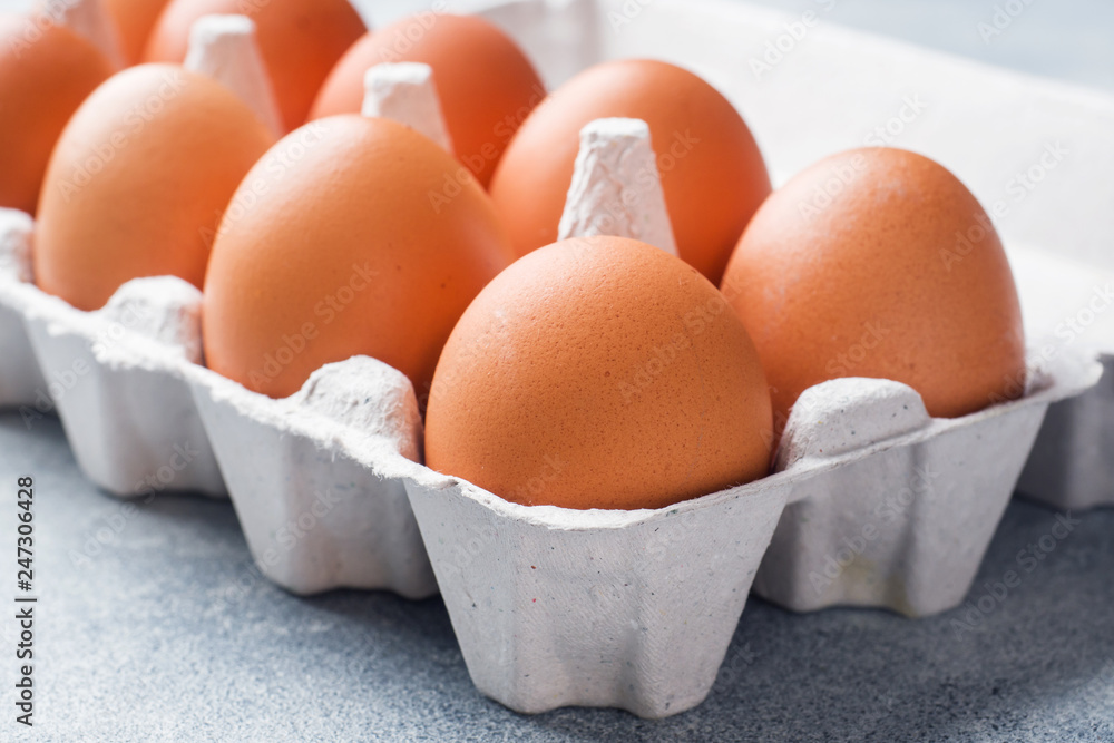 Brown raw Chicken eggs in factory packaging on grey background.