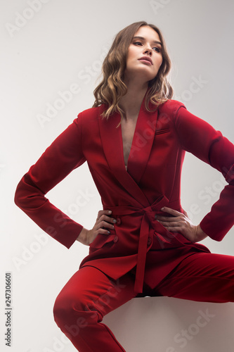 vogue model seating on white cube in red elegant suit