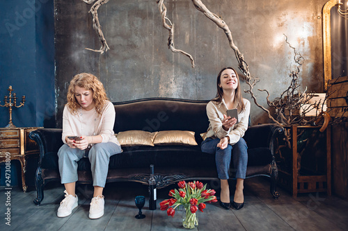 Two young women friends or sisters use social networks on the phone with a completely different emotions