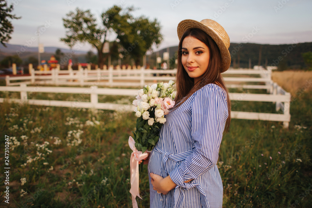 Obraz premium Back view of pregnant woman. She hold a bouquet of flowers and smile