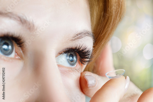 A closeup of a woman inserting a contact lens into her eye.