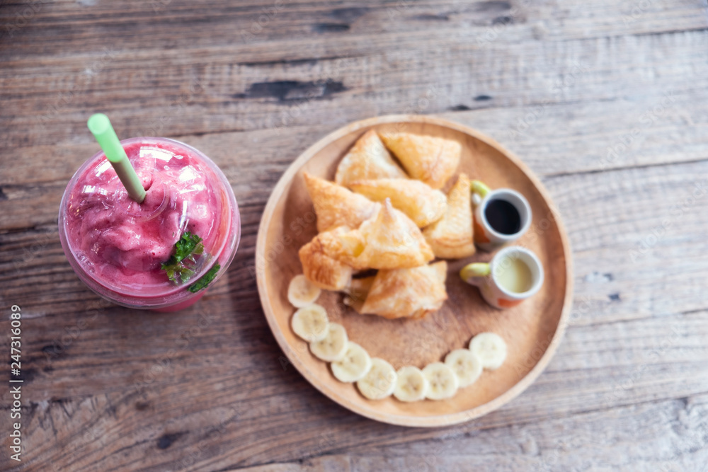 Blurred for Background.Fried Roti with banana on brown wooden plate and Smoothie Strawberry.