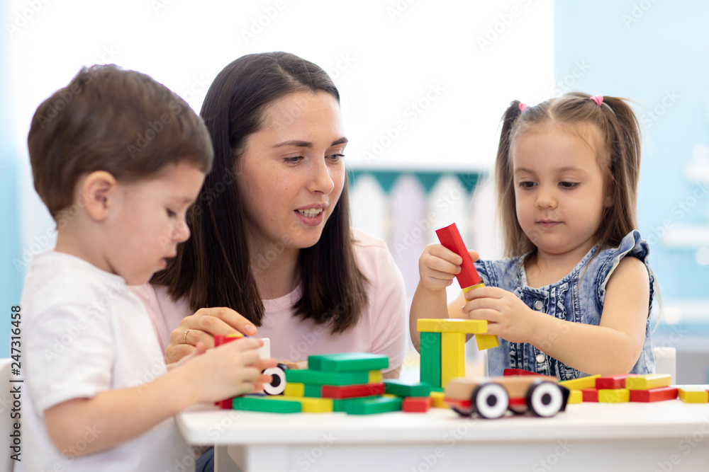 Mother or teacher with children building block toys at home or daycare. Kids playing with color blocks. Educational toys for nursery and kindergarten. Mother or teacher with children building block toys at home or daycare. Kids playing with color blocks. Educational toys for nursery and kindergarten.