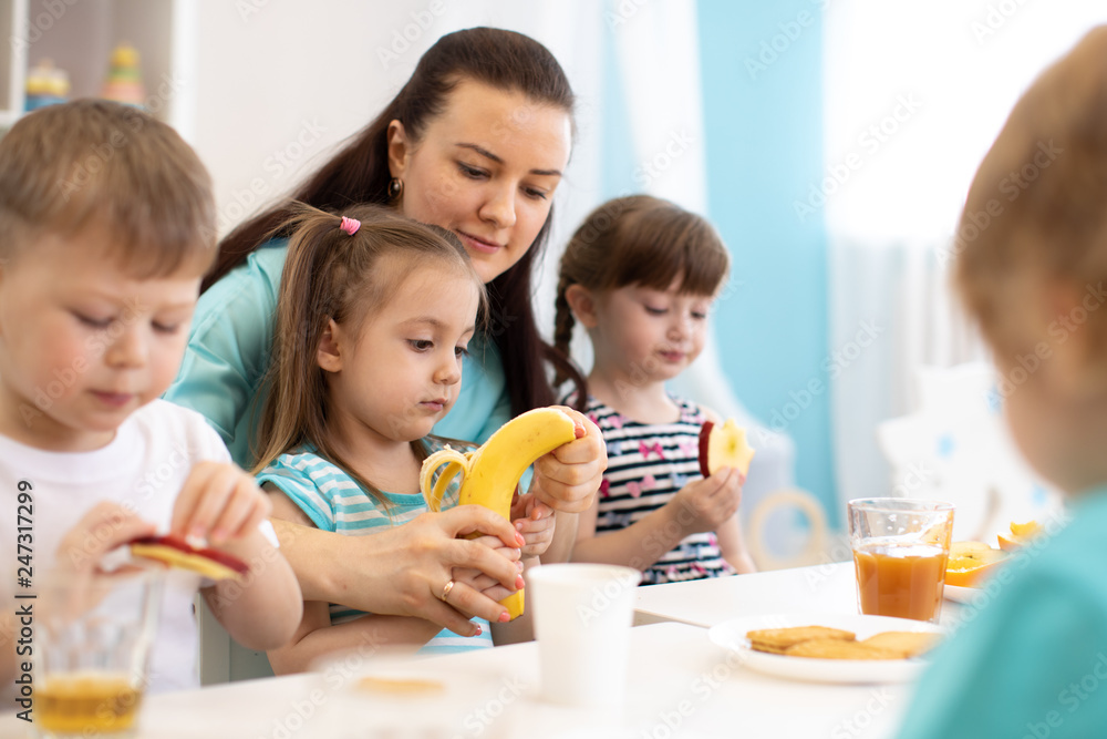 Kids have lunch. Children and carer together eat fruits in kindergarten or day care center Kids have lunch. Children and carer together eat fruits in kindergarten or day care center