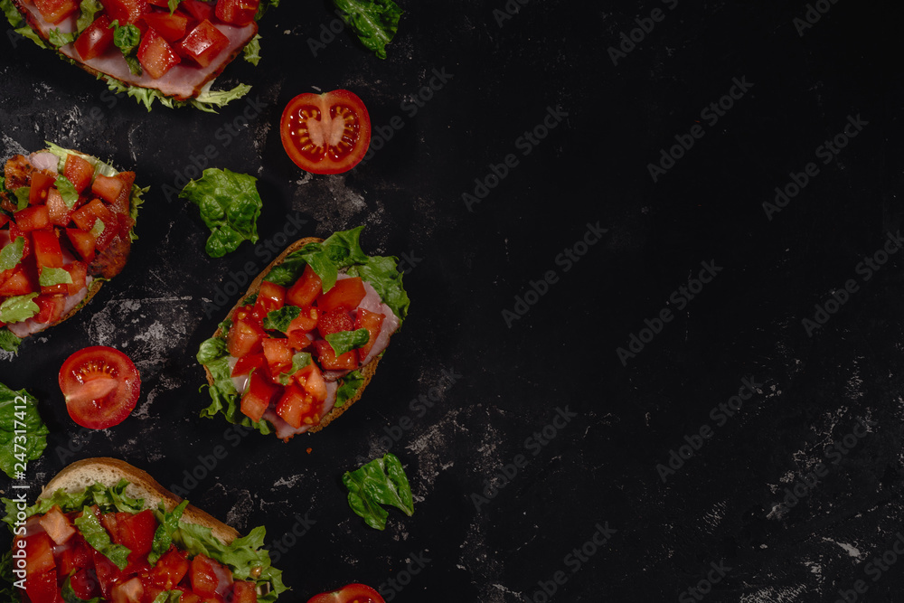 Traditional Italian Bruschetta with tomatoes, sauce, salad leaves and ham on a dark baton background. Traditional Italian appetizer or snack, antipasto. Top view with copy space, copy-paste. Flat lay Traditional Italian Bruschetta with tomatoes, sauce, salad leaves and ham on a dark baton background. Traditional Italian appetizer or snack, antipasto. Top view with copy space, copy-paste. Flat lay