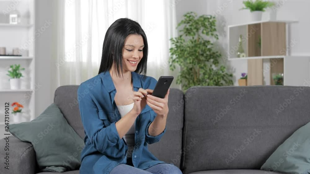 Happy woman using a smart phone sitting on a sofa in the living room at home Happy woman using a smart phone sitting on a sofa in the living room at home