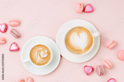 Coffee cups with candys and macaroons on pale pink background. Flat lay, top view