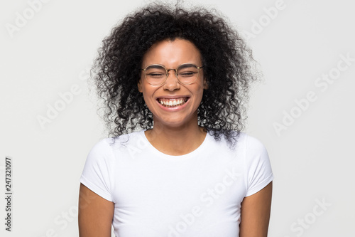 Funny african woman wearing glasses laughing at humor joke isolated on white grey studio background, happy cute black girl with afro hair having fun feeling joy enjoy laughter and positive emotions
