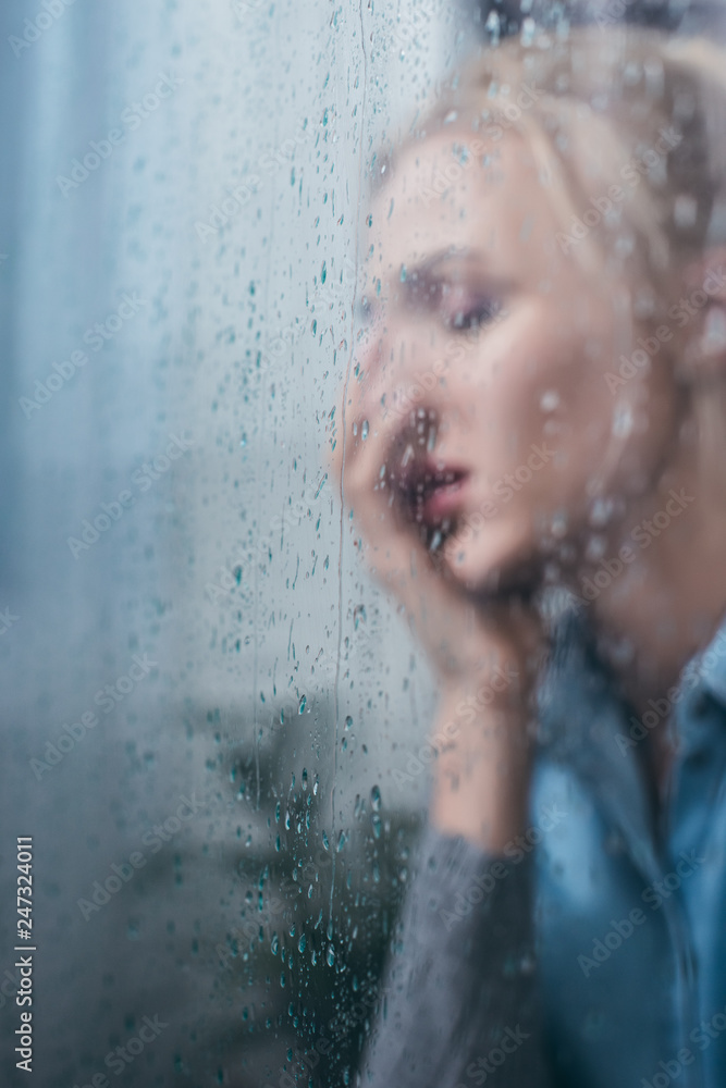 Fototapeta premium selective focus of sad woman covering face with hand through window with raindrops and copy space