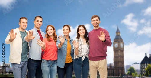 friendship and people concept - group of smiling friends waving hands over london city background