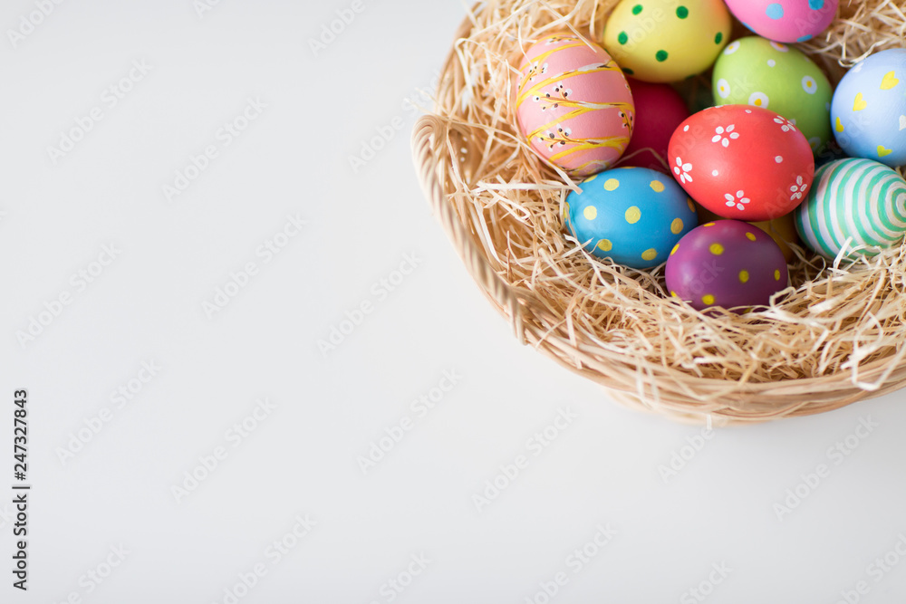 easter, holidays, tradition and object concept - close up of colored eggs in wicker basket on white background