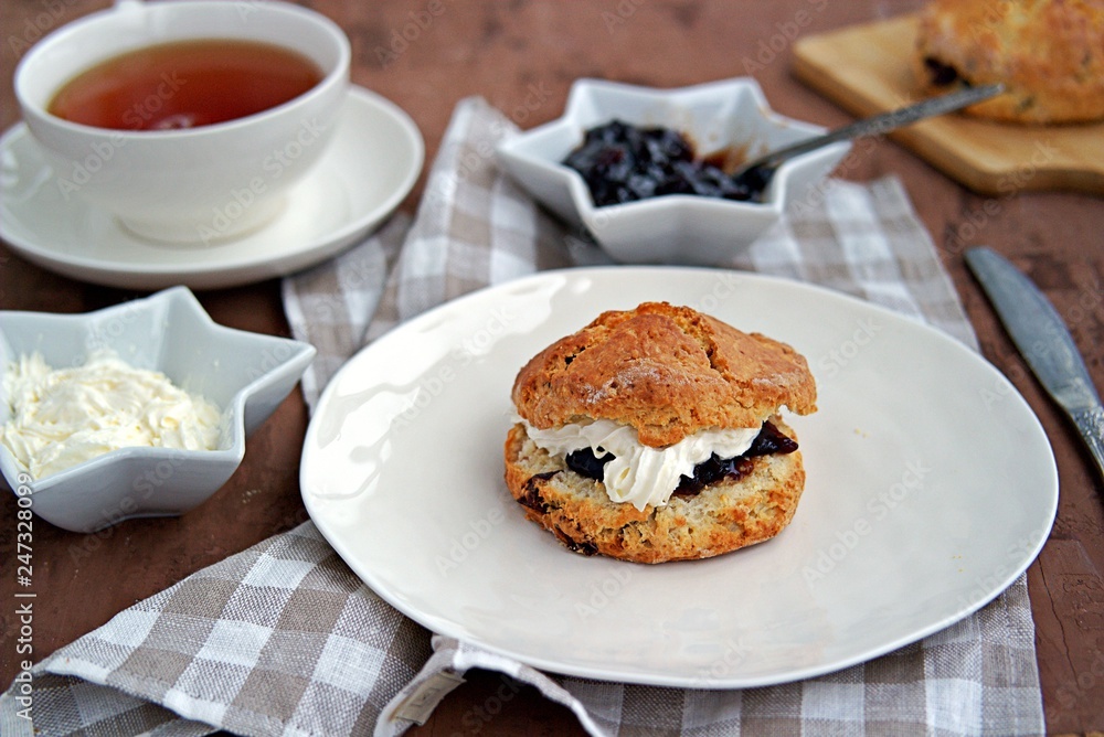 Traditional English scones with dried cranberries on a white plate. Served with jam and whipped cream. Traditional English scones with dried cranberries on a white plate. Served with jam and whipped cream.