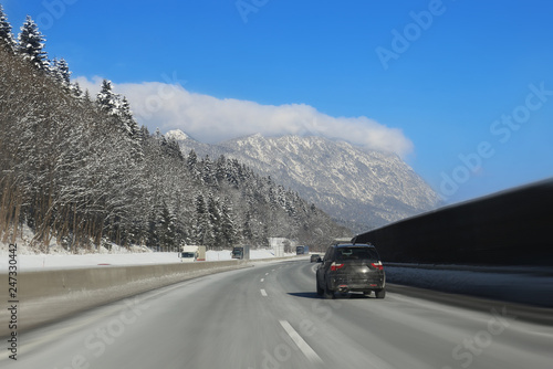 Car running on curve of empty winter highway road with beautiful mountains covered with snow on background. Winter travelling and vacation