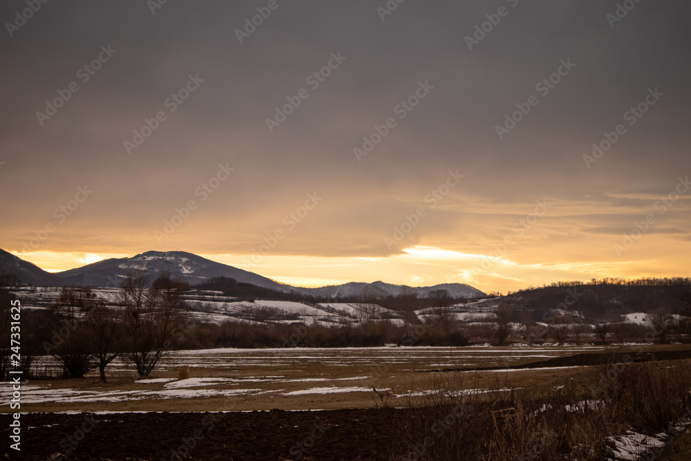 Winter sunset with mountains and meadows in the background and little bits of snow