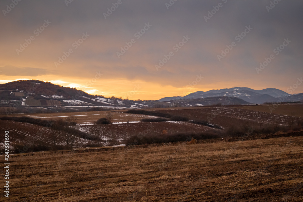 Winter sunset with mountains and meadows in the background and little bits of snow