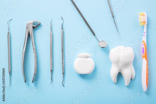 Dental health and teethcare concept. Professional steel dental instruments with a mirror near white tooth model, toothbrush and dental floss on light blue background. © Nikolay N. Antonov