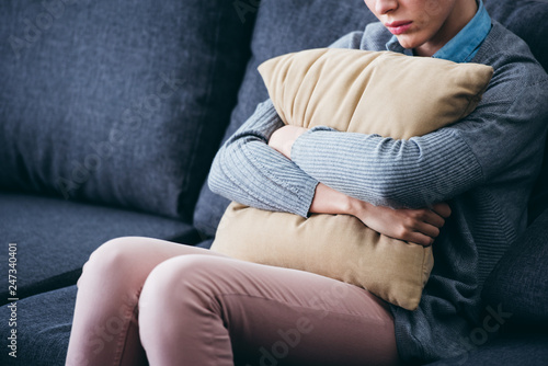 cropped view of woman sitting on couch and holding pillow at home