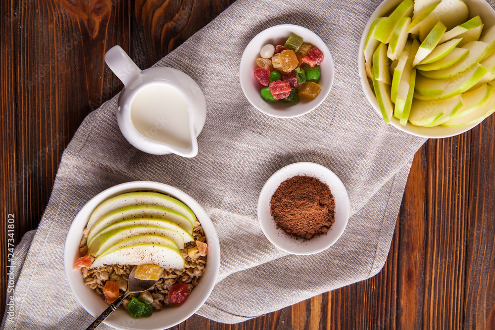 Breakfast bowl of oat granola with apple and dry fruit in a white bowl on brown wooden background with a yogurt. Copy space Breakfast bowl of oat granola with apple and dry fruit in a white bowl on brown wooden background with a yogurt. Copy space
