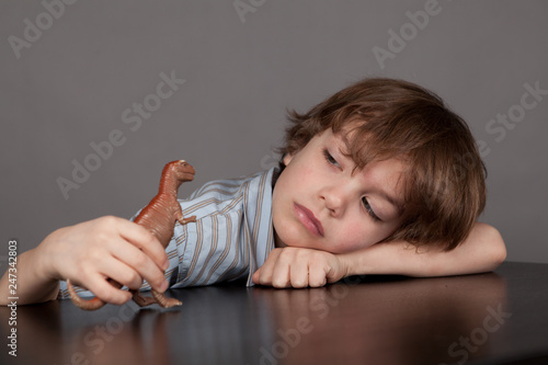 Thinking student sitting at desk and plays with dinosaur