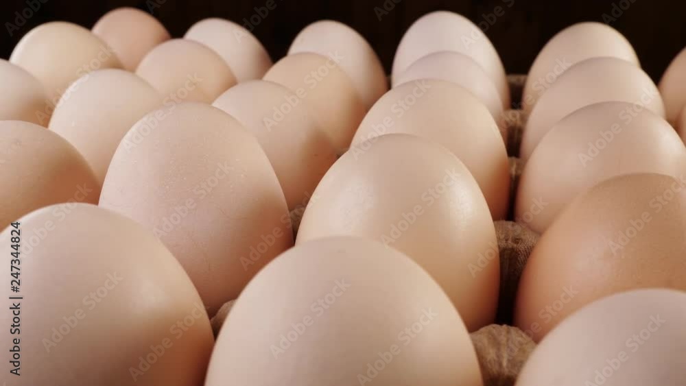 Fresh uncooked large chicken eggs in a paper box rotate on a stand. Fresh uncooked large chicken eggs in a paper box rotate on a stand.