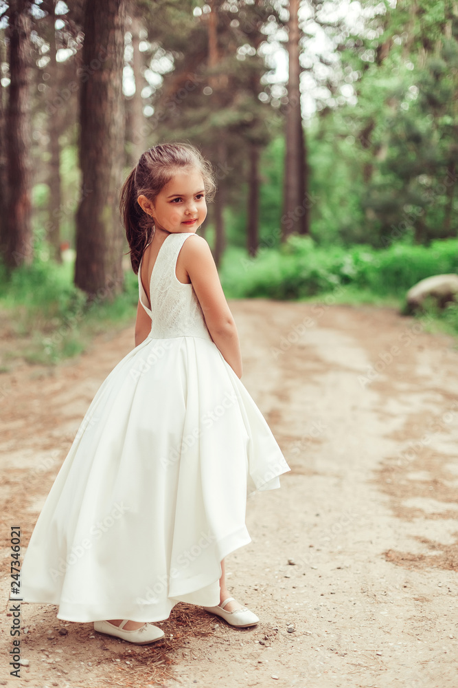 Outdoor portrait of cute brunette emotional girl dancing and having fun in elegant fashionable dress. Childhood, nature, fashion concept