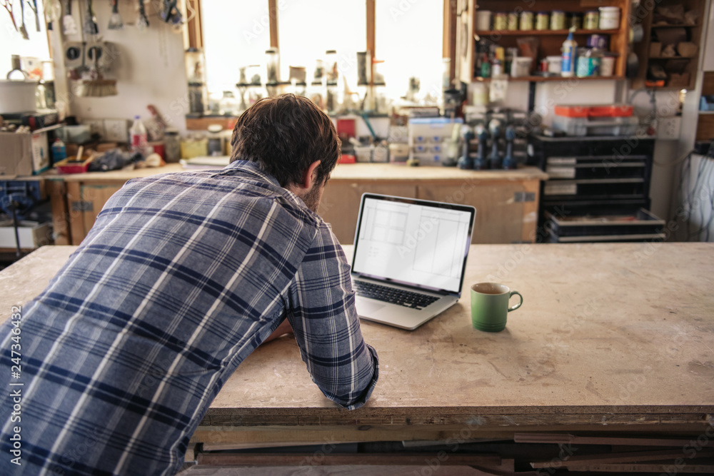 Woodworker working online with a laptop in his workshop Woodworker working online with a laptop in his workshop