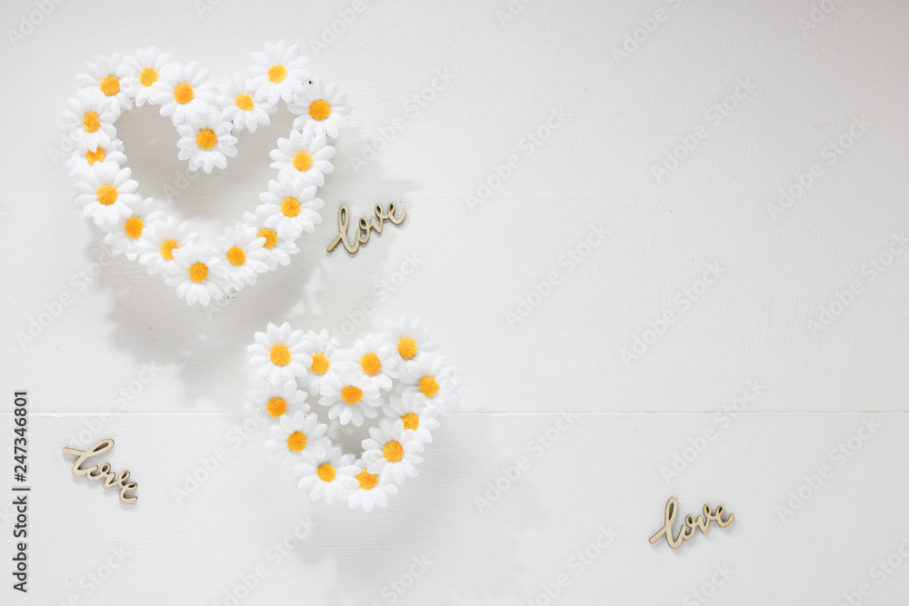 Two Hearts of Daisy Chain Flowers and Word LOVE are on White Wooden Background. One Heart is Bigger in Size than the Other. It`s Symbol of Male & Female or Adult & Child. Concept: Love.