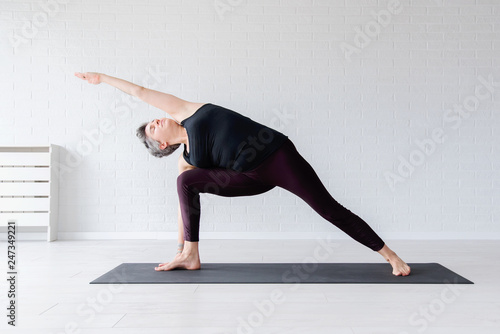 Mature Caucasian woman practicing yoga on livingroom floor. Middle aged woman doing yoga indoors.