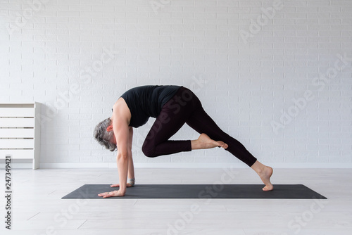 Mature Caucasian woman practicing yoga on livingroom floor. Middle aged woman doing yoga indoors.