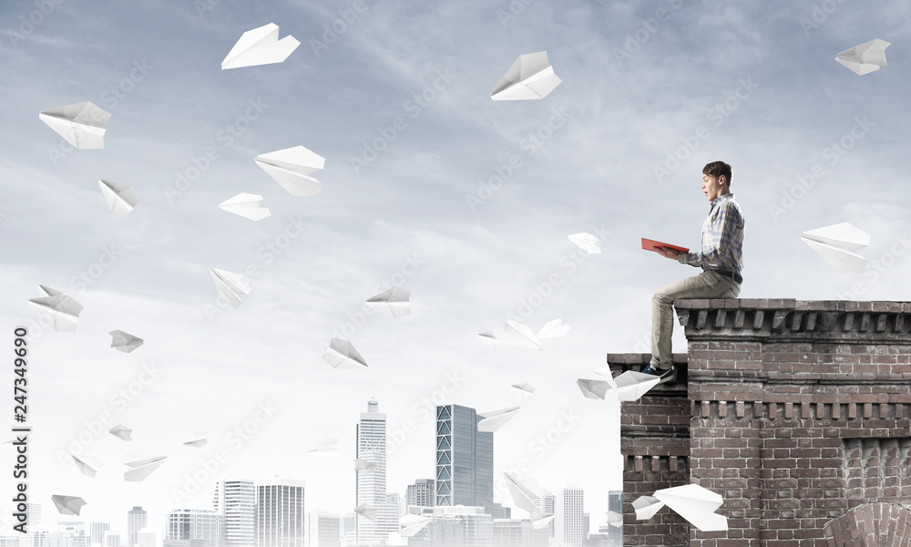 Handsome student guy on roof edge reading book and paper planes fly around Handsome student guy on roof edge reading book and paper planes fly around