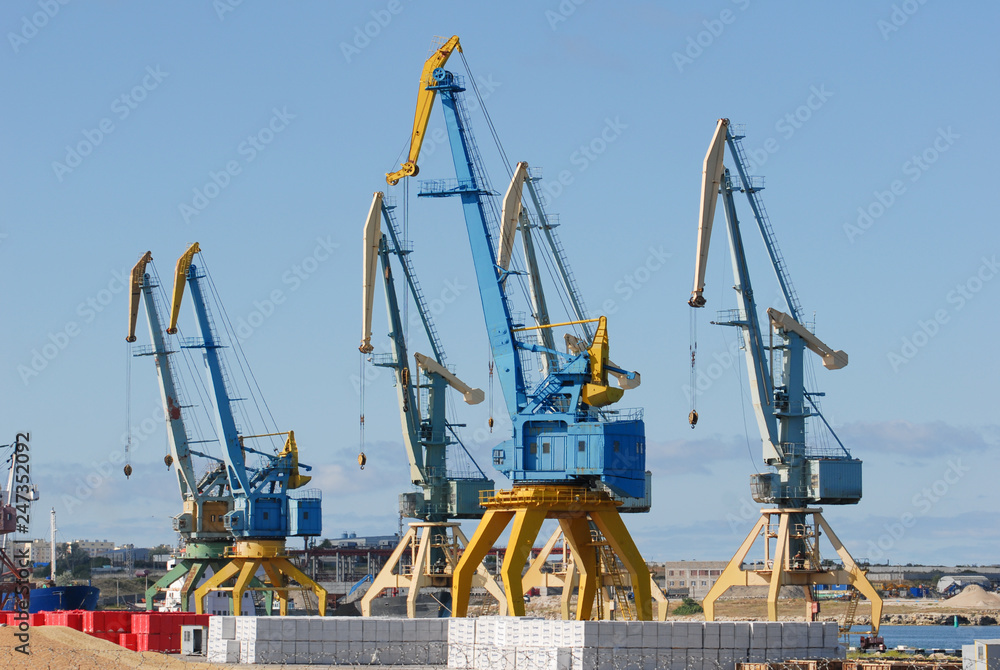 high tower cranes in sea port with products on blue sky background