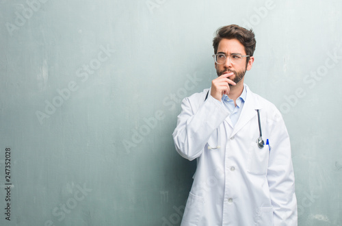 Young friendly doctor man against a grunge wall with a copy space doubting and confused, thinking of an idea or worried about something
