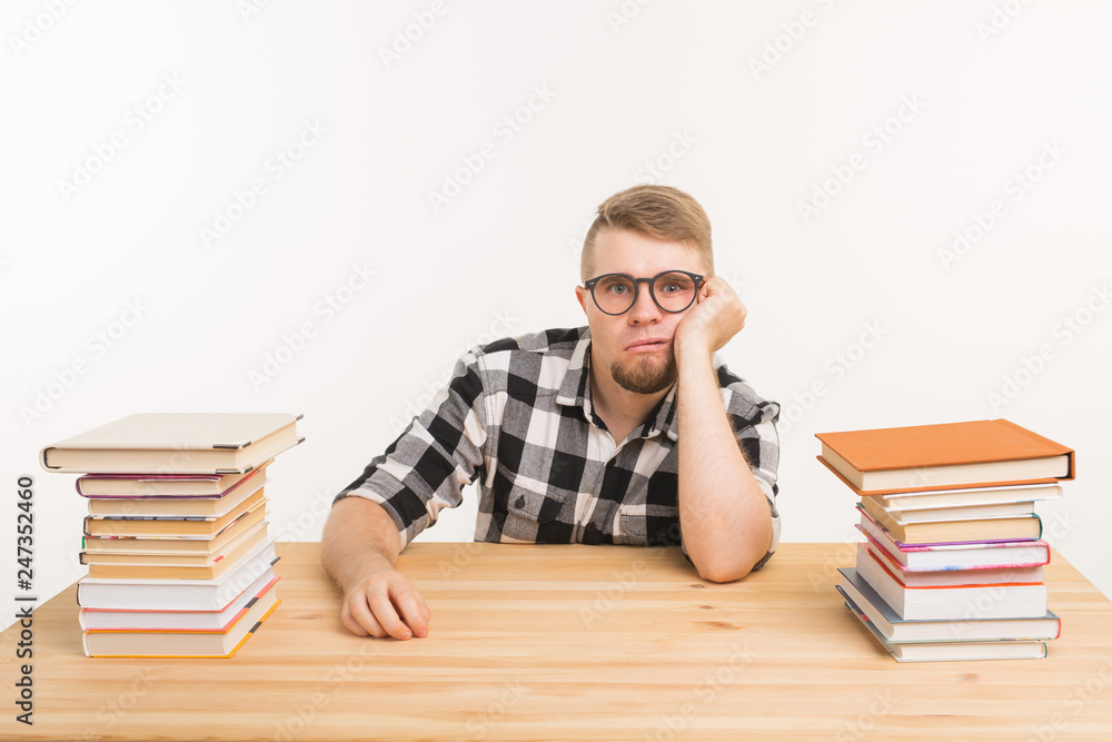 People, knowledge and education concept - Tired male student sitting at the table with mountains of books and does not want to study up People, knowledge and education concept - Tired male student sitting at the table with mountains of books and does not want to study up