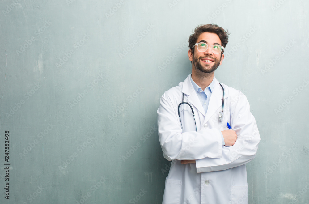 Young friendly doctor man against a grunge wall with a copy space looking up, thinking of something fun and having an idea, concept of imagination, happy and excited Young friendly doctor man against a grunge wall with a copy space looking up, thinking of something fun and having an idea, concept of imagination, happy and excited