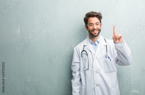 Young friendly doctor man against a grunge wall with a copy space showing number one, symbol of counting, concept of mathematics, confident and cheerful