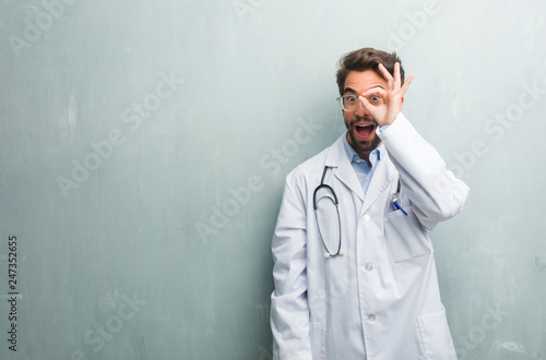 Young friendly doctor man against a grunge wall with a copy space cheerful and confident doing ok gesture, excited and screaming, concept of approval and success