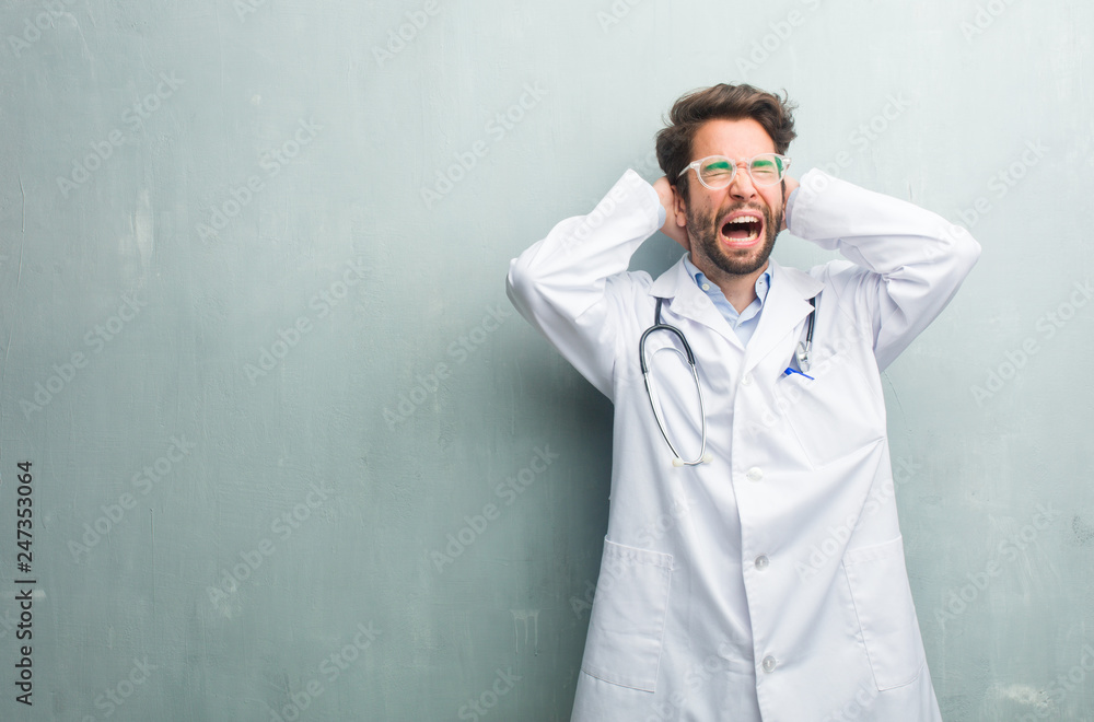 Young friendly doctor man against a grunge wall with a copy space crazy and desperate, screaming out of control, funny lunatic expressing freedom and wild Young friendly doctor man against a grunge wall with a copy space crazy and desperate, screaming out of control, funny lunatic expressing freedom and wild