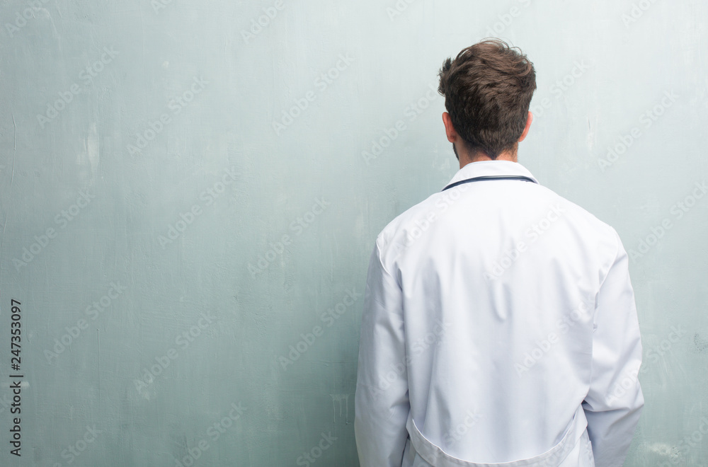 Young friendly doctor man against a grunge wall with a copy space showing back, posing and waiting, looking back Young friendly doctor man against a grunge wall with a copy space showing back, posing and waiting, looking back