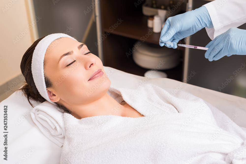beautician holding syringe in front of woman face at beauty salon