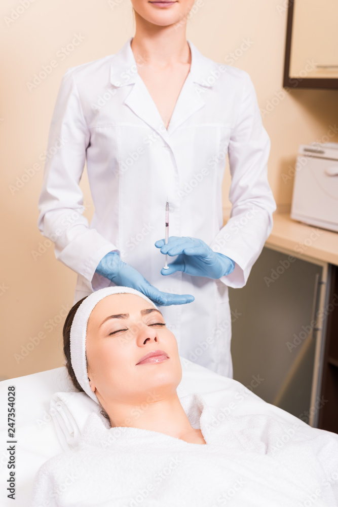 Obraz premium woman lying on massage table while beautician preparing injection in syringe at beauty salon