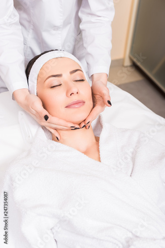 cosmetologist doing manual massage on woman face at beauty salon